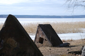 Triangular concrete structures on the river bank. On river near the shore there are two concrete structures in the form of triangles. In the distance yellow reeds on the water ice on the shore sand.