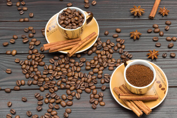 Ground coffee and roasted coffee beans in cups. Cinnamon sticks on saucer. Coffee beans and star anise on table