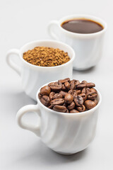 Three white cups with coffee beans, ground coffee and coffee drink.