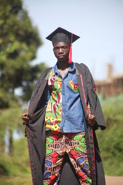 Black African American Young Man Cerebrates His Graduation With A Photo Shoot In The Middle Of The Road Wearing The Gown And In The African Traditional Clothes