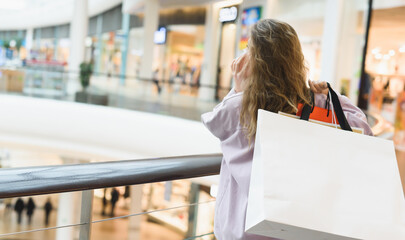 Shopping mall. A young woman holding a lot of shopping bags and talking phone.