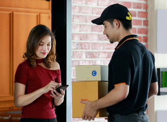 Beautiful Asian female customer signs electronic signature on mobile device while receiving...