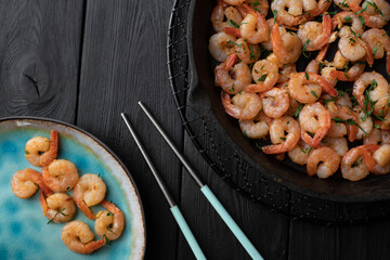 Prawns fried with garlic on a blue porcelain plate and in a black cast iron skillet with chopsticks...