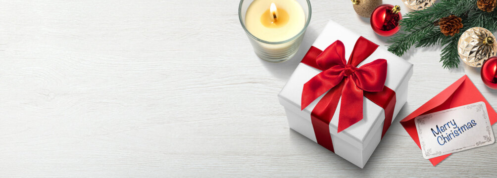  白木のテーブルの上に置かれたクリスマスプレゼントの箱、メッセージカード、キャンドル、クリスマスオーナメント。