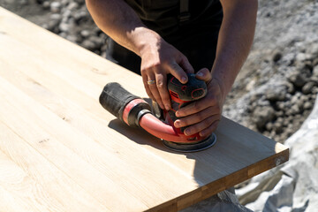construction worker using a cordless power sander to sand a massive wooden table top
