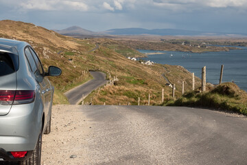 Rented car parked off road with epic view on a mountains. Sky road, near Clifden town, county Galway, Ireland. Warm sunny day with cloudy sky. Travel and tourism concept.