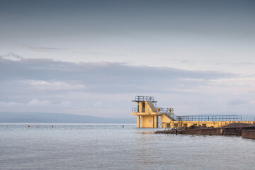 Fototapeta na wymiar Blackrock public diving board. Salthill beach, Galway city, Ireland. Popular town landmark and swimming place. Calm morning light and blue cloudy sky, High tide