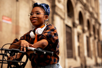 Fototapeta na wymiar Happy young woman riding bicycle in the city. Woman with headphones enjoying outdoors