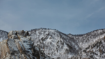Fototapeta na wymiar A flat-topped rock devoid of vegetation. Cracks on the stones. Background - wooded snow-covered hills, blue sky. Close-up. Baikal