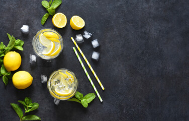 Cold lemonade with mint and ice on a black concrete background, top view.