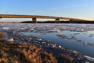 Beautiful evening landscape at sunset with a view of the bridge over the river during the spring ice drift.