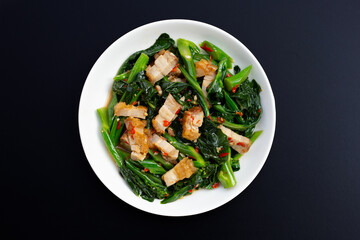 Stir fried chinese kale with crispy pork belly, Dark wooden background.