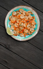 Prawns fried with garlic on a blue porcelain plate with a slice of lime on a black wooden table. Vertical photo. Top view
