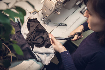 Seamstress sews clothes and cuts the seam on a fashionable jacket made of velvet fabric, on a sewing machine in her studio, top view