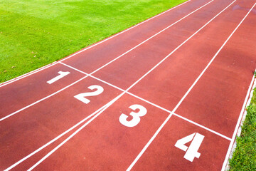 Aerial view of sports stadium with red running tracks with numbers on it and green grass football field.