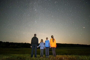 Happy family standing in night field looking at dark sky with many bright stars. Parents and...
