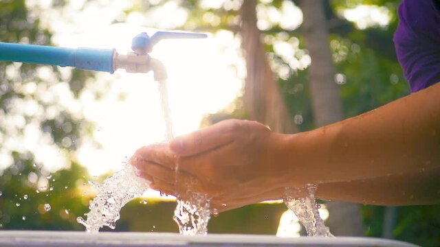 Man hands holding in freshwater flowing from faucet. Water conservation concept. Slow motion shot