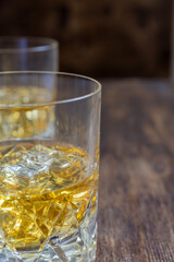 Close-up of two glasses with whiskey on ice, selective focus, on dark wooden table, vertical, with copy space