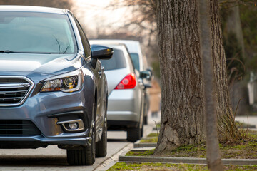 Cars parked in a row on a city street side on bright autumn day.