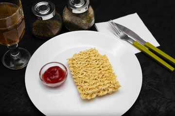Dry instant noodles in a white plate. Cheap food concept. Beautifully decorated dish with ketchup,...
