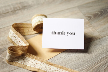 White thank you card on wooden background with a natural paper envelope and burlap ribbon. Special thank you note.