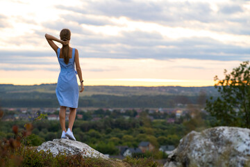 Naklejka premium A young woman in summer dress standing outdoors enjoying view of bright yellow sunset.