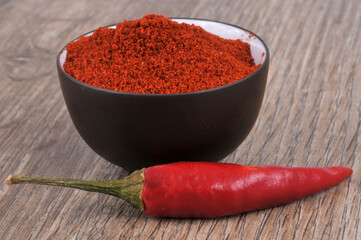 Bol de piment en poudre et piment rouge en gros plan sur fond en bois