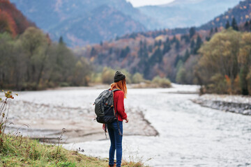 woman hiker with raised hands on the river bank in the mountains in autumn on nature