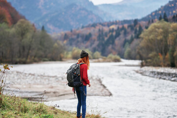 Obraz premium woman hiker with raised hands on the river bank in the mountains in autumn on nature