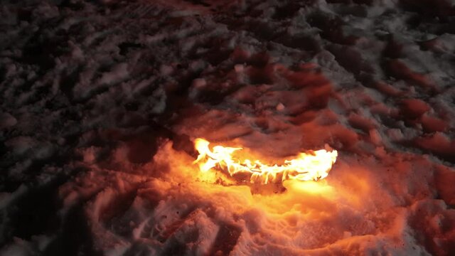 Burning sword lies on the snow after the battle is over. Winter night low light.