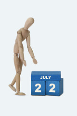day of the month 22 July calendar . A calendar date on blue cubes and a wooden man standing next to it. White background