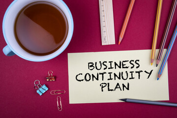BUSINESS CONTINUITY PLAN. Note sheet and office supplies on a red background