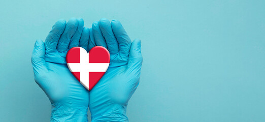 Doctors hands wearing surgical gloves holding Denmark flag heart
