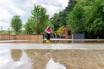 child girl playing with paper boat in a large puddle, copy space