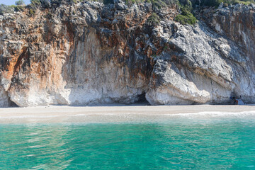 Turquoise sea, cliffs surrounded by green plants and a tourist tent on a small wild beach, Albania. Travel theme, beautiful nature