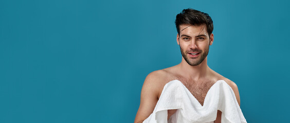 Studio portrait of cheerful brunette guy using a white towel to wipe himself after shaving and...