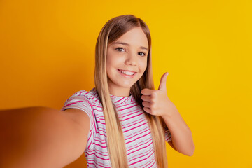 Little kid girl make photo selfie show thumbup sign isolated over yellow background