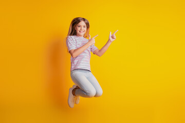 Photo of jumping high schoolgirl point finger empty space isolated on yellow background