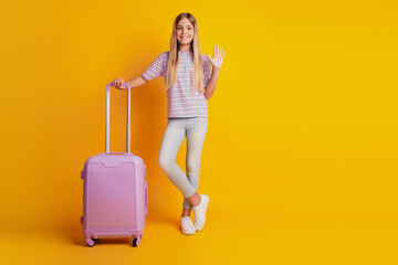 Pretty little kid girl isolated on yellow background hold suitcase wave hand