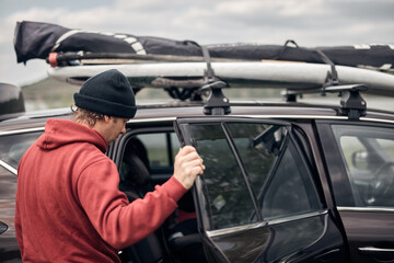 Windsurfer and camper packing and unpacking from a car's roof rack in nature.