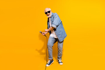 Full length body size of overjoyed grandfather in sunglass dancing with microphone on stage isolated vibrant yellow color background