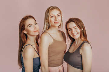 Three girls in comfortable home clothes together on a pink background. Women smile and have fun. The concept of spa treatments, natural beauty and care, youth, cream and mask, freshness, friendship
