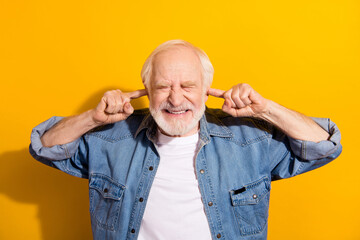Photo of unhappy irritated upset old man close ears fingers bad mood loud noise isolated on yellow...