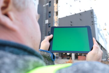Tablet with green screen against the backdrop of a building under construction.