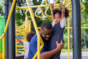 Happy mixed race family in park. African father caring little daughter playing at children...