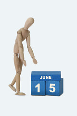 day of the month 15 June calendar . A calendar date on blue cubes and a wooden man standing next to it. White background