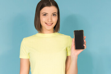 Caucasian teen girl holding cell phone mockup , smiling, isolated on blue background