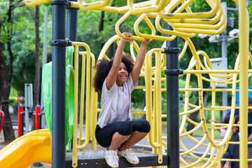 Happy mixed race family in park. Adorable child girl kid playing and hanging on jungle gym at children playground. Little daughter enjoy and having fun outdoor lifestyle weekend activity in summer. - Powered by Adobe