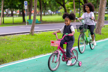 Happy mixed race family in park. Two Adorable little sibling sister learning ride bicycle together...