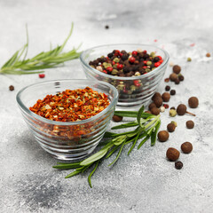 dried tomatoes, garlic and basil spices in the bowl with colorful pepper at the background and branches of rosemary at the grey beton background